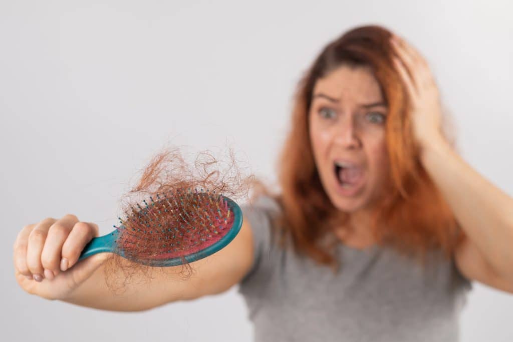 ¿Qué vitaminas tomar para la caída del cabello? 1 Mujer sorprendida al ver la cantidad de cabello que se le cae al cepillarse