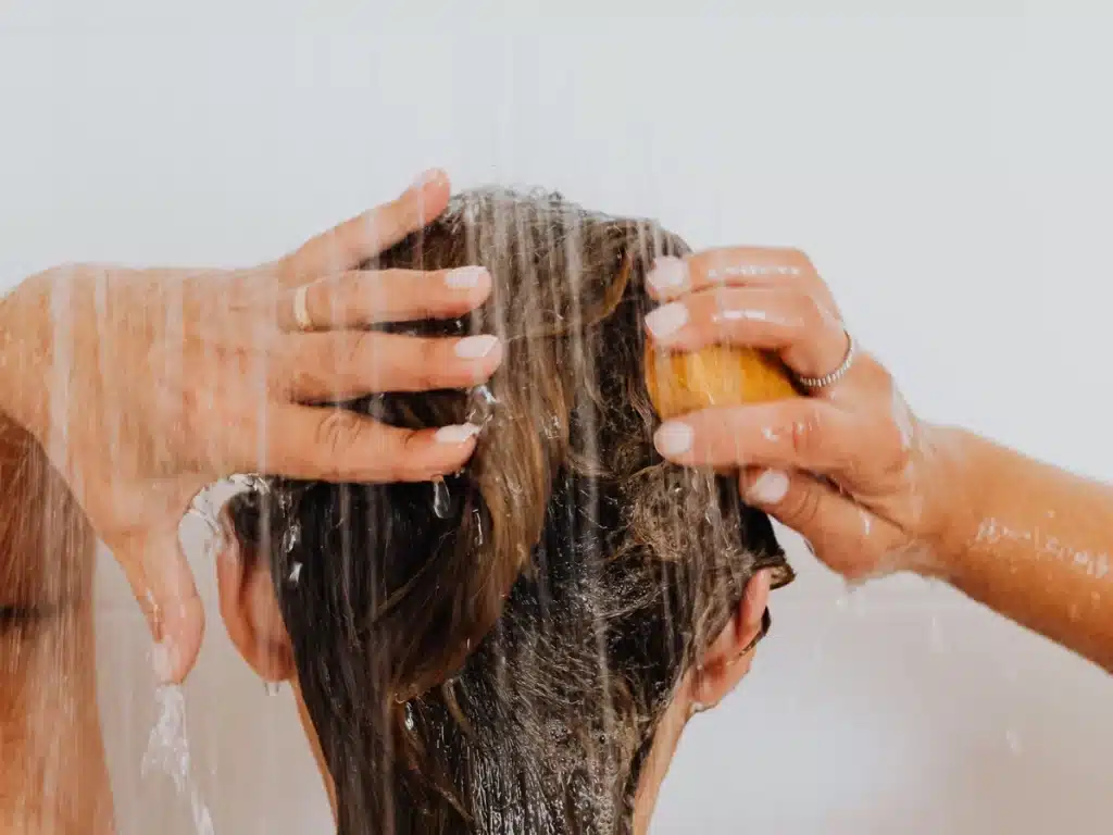 El agua caliente daña el cabello persona lavando el cabello mientras el agua caliente cae sobre el cuero cabelludo